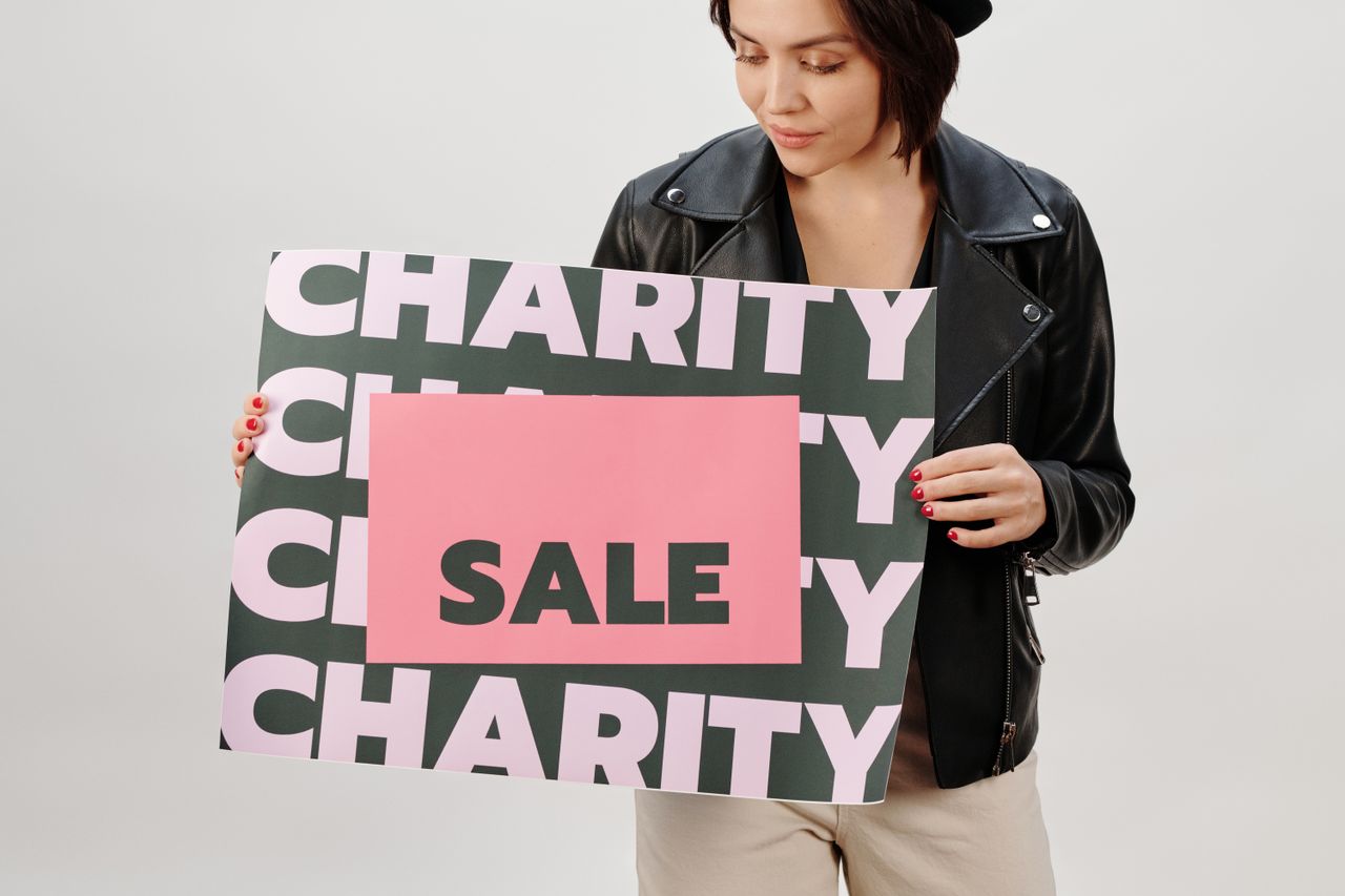 A woman in a studio holds up a sign for a charity sale.